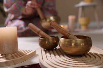 Woman with singing bowls and burning candles indoors, selective focus