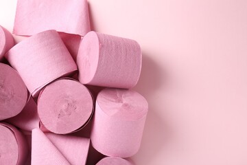 Color toilet paper rolls on light pink background, top view. Space for text