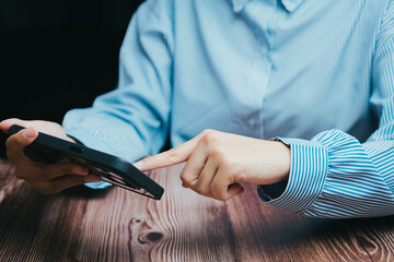 Naklejka premium Person Using Smartphone on Wooden Table in Bright Indoor Setting, Business concept
