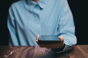 Person Holding Smartphone in Dark Background with Wooden Table, Business concept