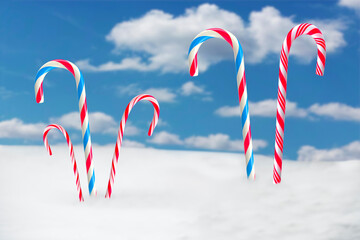Colorful striped red white and blue christmas candy canes in snow against blue sky with clouds