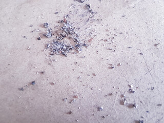 Close-up photograph captures a scattering of cigarette ash on a pale surface, possibly skin. The ash appears as a mix of gray, black, and white particles, with a grainy texture that contrasts wit
