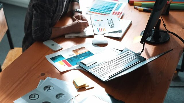 Interior designer looking at laptop and designing color while looking at palette at meeting table with laptop, computer and paper placed. Close up of business man working on color design. Symposium.