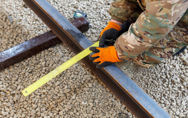 A man in a camo jacket is measuring a rail with a yellow tape measure