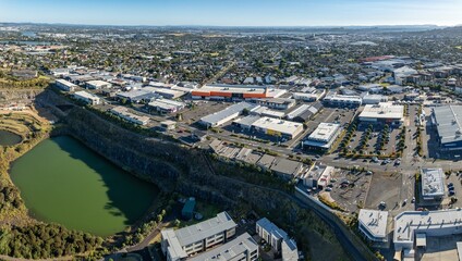 Fototapeta premium Aerial view of a bustling shopping center and residential area. Retail stores, parking lots, and homes are visible. Urban development. STONEFIELDS, AUCKLAND, NZ