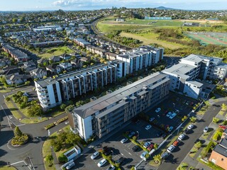 High-angle view of modern apartment complex nestled within residential neighborhood. Parking lots and streets are visible. Urban development. STONEFIELDS, AUCKLAND, NZ