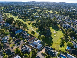 Aerial view of a residential neighborhood bordering a golf course. Homes and lush green spaces blend seamlessly. ST JOHNS, AUCKLAND, NZ