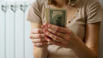 A person counts a stack of cash while sitting in a comfortable indoor space. The focus is on the hands handling the money, reflecting a moment of financial consideration.