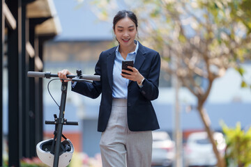 Young businesswoman is using her smartphone while holding an electric scooter, showcasing modern commuting and technology in an urban environment