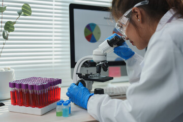 Scientist wearing gloves and protective glasses analyzes samples under a microscope in a laboratory...