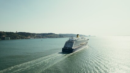 Fototapeta premium Multi-storey motor ship sails along a wide river towards the sun, drone video