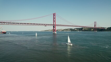 The drone flies over the wide Tagus River in Portugal, with a red suspension bridge connecting Lisbon and Almada