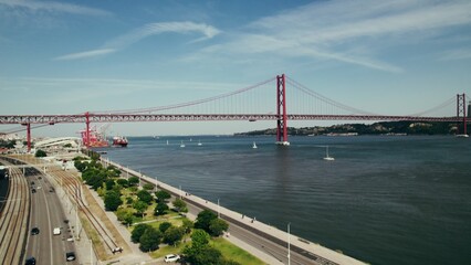 The drone flies over the wide Tagus River in Portugal, with a red suspension bridge connecting Lisbon and Almada