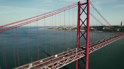 A bird's-eye view of a red suspension road bridge over a wide river with cars passing on them. Drone video on a summer day