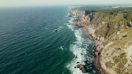 Bird's-eye view of the sea with rocks on the shore, the tops of which are covered with grass