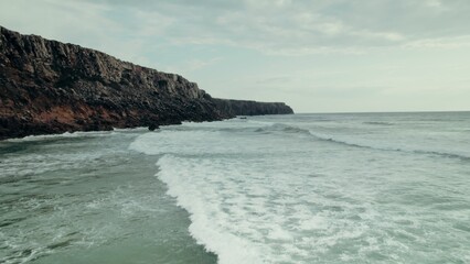 A rocky cliff on the seashore. The sea waves are beating against the rocks. Drone video
