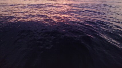 The sea distance at sunset, there is no shore, the drone flies over the water reflecting the pink color of the sky