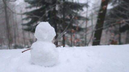 A charming little snowman crafted from snow, nestled in a serene, snow-covered forest during...