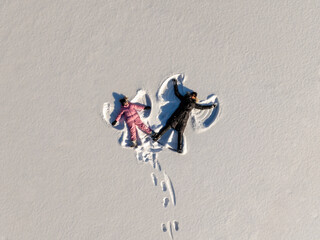 Mother and daughter lie in the snow and make angel figures, photo taken from a drone.