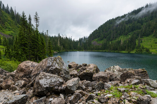 This captivating image depicts a serene lake surrounded by rugged rocky terrain and tall evergreen trees, capturing nature's untouched beauty in a peaceful setting.