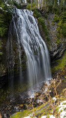 A picturesque waterfall cascades down a rocky surface, enveloped in vibrant green foliage, exemplifying the beauty of nature and the soothing sounds of flowing water.