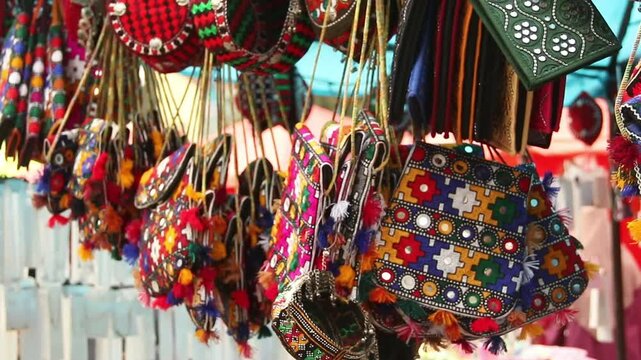 Colorful embroidered textile bag with geometric and floral patterns, orange and purple tones, fringed edges. 
