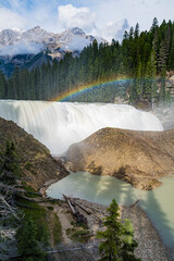 An awe-inspiring waterfall cascades down with a vivid rainbow arcing over, surrounded by lush...