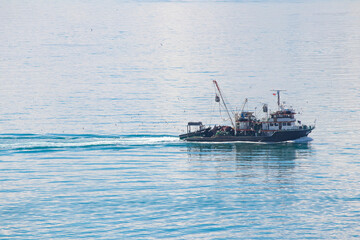 Fishing boat sailing in the blue sea. Minimal and horizontal photo. Watercraft idea concept. Seafood industry. Copy space, blank, empty.