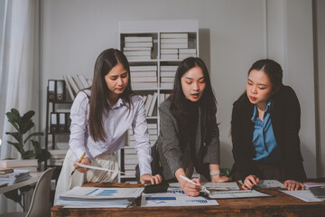 Three asian businesswomen are collaborating on a project, analyzing financial charts and discussing strategies in a modern office setting, demonstrating teamwork and expertise