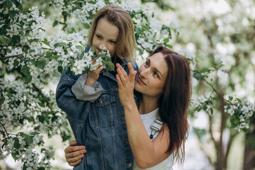 Obraz premium Mother and daughter happy together against the background of blooming apple trees in the garden