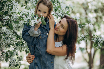 Obraz premium Mother and daughter happy together against the background of blooming apple trees in the garden