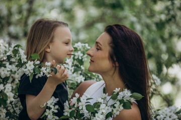 Naklejka premium Mother and daughter happy together against the background of blooming apple trees in the garden