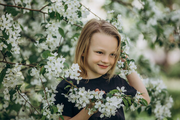 Fototapeta premium A sweet beautiful child girl against the background of blooming apple trees in the garden