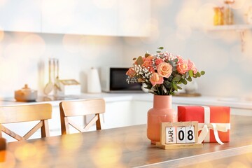Calendar with date of International Women's Day, gift and roses flowers on table in kitchen