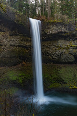 A breathtaking waterfall cascading down rocky cliffs into a serene pool, showcasing the enchanting beauty of nature and the tranquility of forested landscapes.