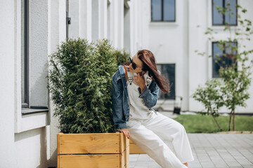 Fototapeta premium An adult young beautiful female model in a jacket, overalls and sunglasses walks around the city