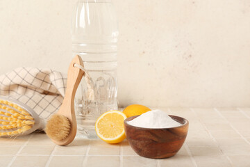 Bowl of baking soda, vinegar, cleaning brushes and lemons on light tile table