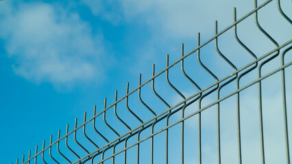 green fence made of 3d mesh panels close-up on blue sky background