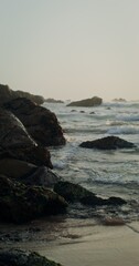 Foamy sea waves beat against the rocks on the shore at sunset