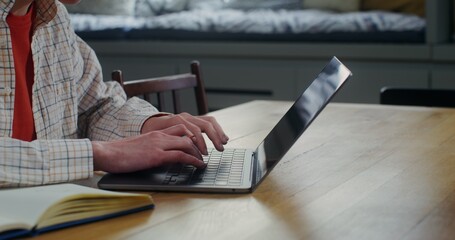 A young woman is smiling typing on a laptop at home. The video moves from the woman's hands to her face. Remote workplace