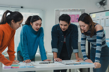 Four young ux designers are examining a new mobile application prototype, discussing different layouts and functionalities in a modern office environment