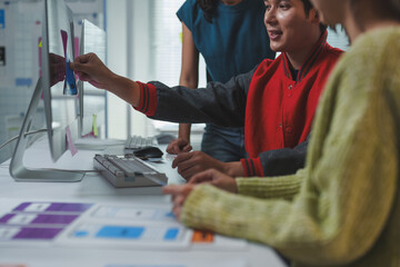Web designers collaborating in a modern office, applying sticky notes to a monitor while planning the layout and user interface for a new website