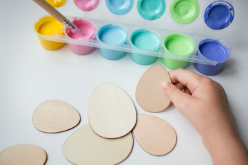 Child hand holding Easter wooden egg shapes with colorful paints for Easter crafting