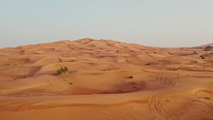 Red desert dunes with sparse vegetation among the sand with traces of cars driving off-road. Drone video