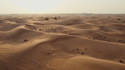 A bird's-eye view from a drone of sand dunes with traces of cars engaged in off-road driving, and sparse vegetation among the sand