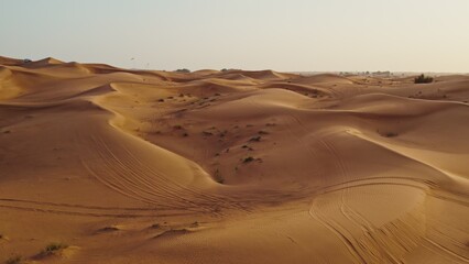 A bird's-eye view from a drone of sand dunes with traces of cars engaged in off-road driving, and sparse vegetation among the sand
