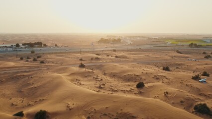 Busy modern highway in the middle of the desert. An oasis among the sands. Cars drive along the highway among the sand dunes. Drone view