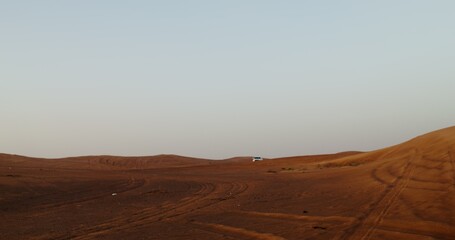 A white SUV is driving among sand dunes in a desert with no roads