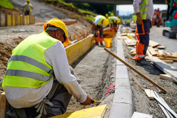 Workers preparing highway shoulder for concrete installation between road curbs and shoulder slope