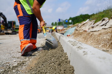 Worker smoothing concrete with a shovel next to road curb at highway construction site © Redline Visuals